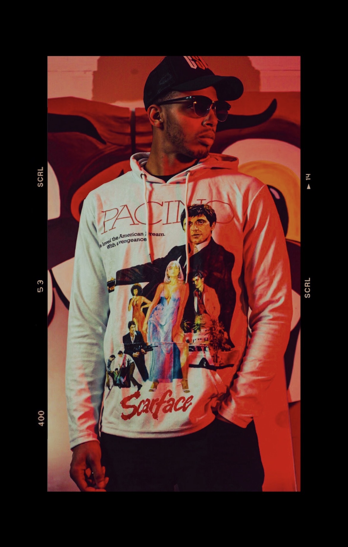 Street style portrait in a Scarface hoodie against a red-lit graffiti mural