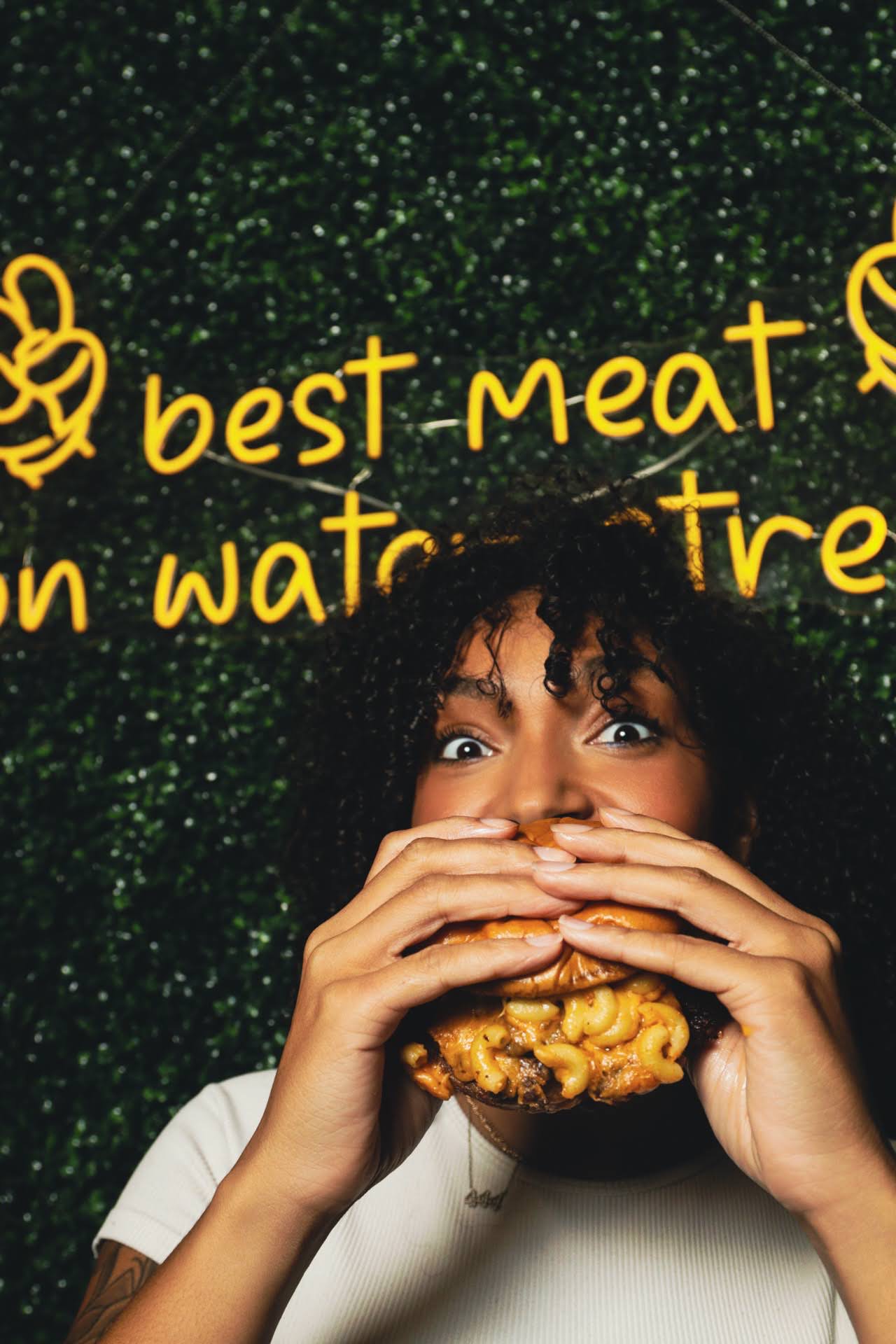 Guest photographed mid-bite with a burger, neon-yellow handwriting on the wall behind her