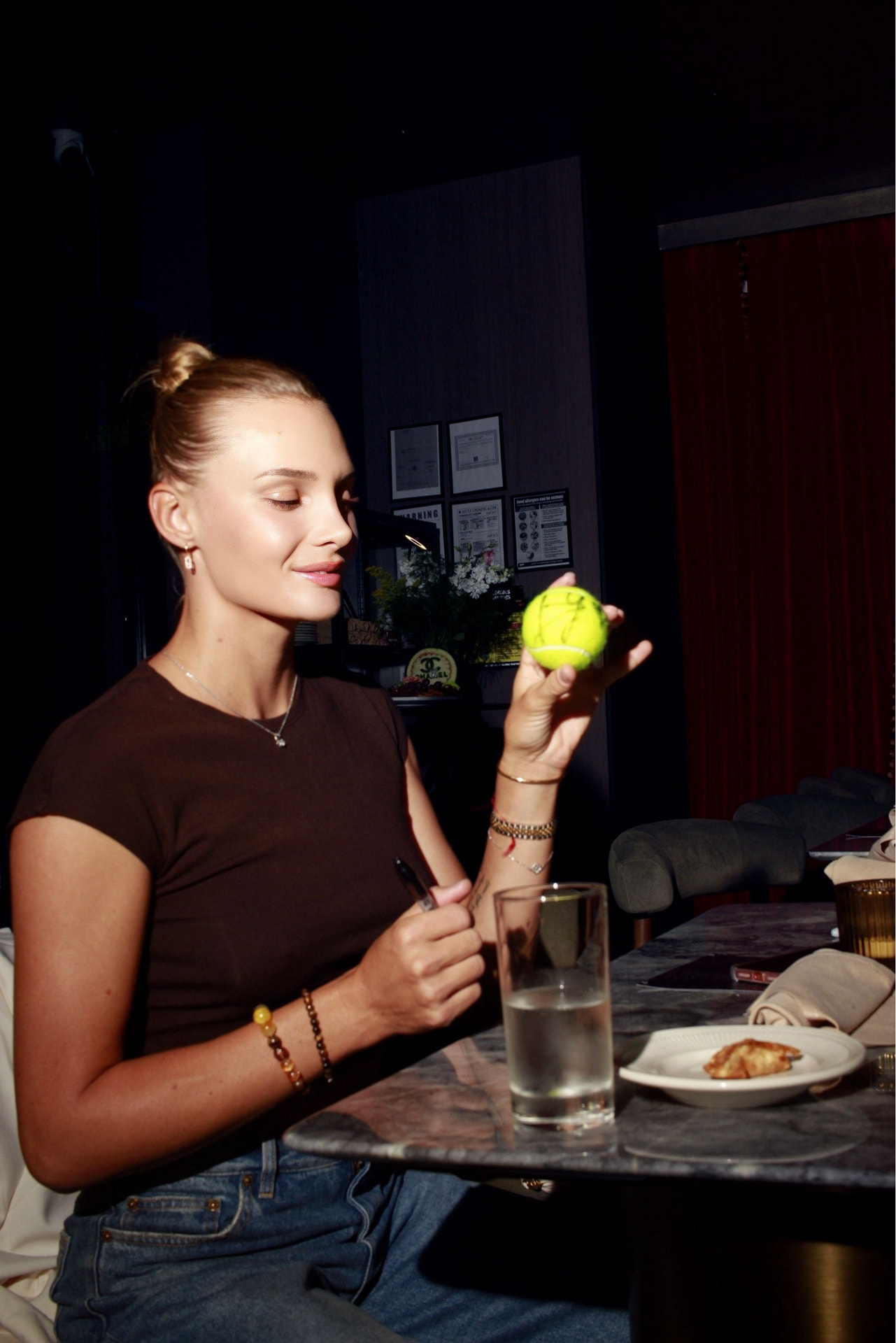 Guest signing a tennis ball at a marble dining table in low light